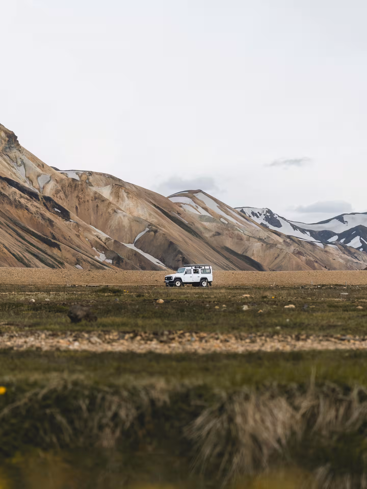 White Land Rover Defender driving across vast Icelandic highland plain with colorful rhyolite mountains behind