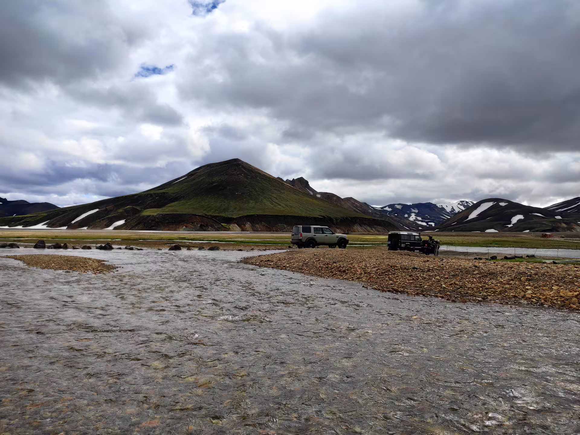 4x4 vehicles crossing a glacial river at Landmannalaugar with colorful rhyolite mountains in Iceland