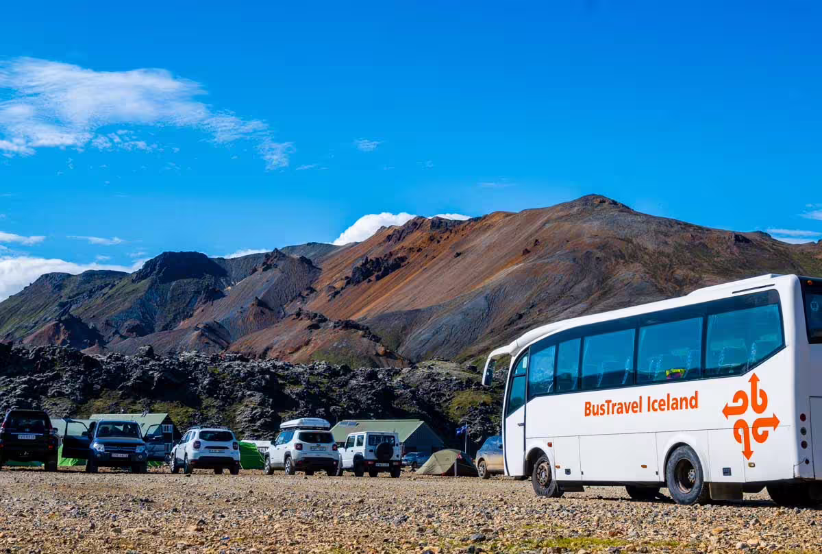 BusTravel Iceland tour bus parked at Landmannalaugar campsite with colorful rhyolite mountains in background