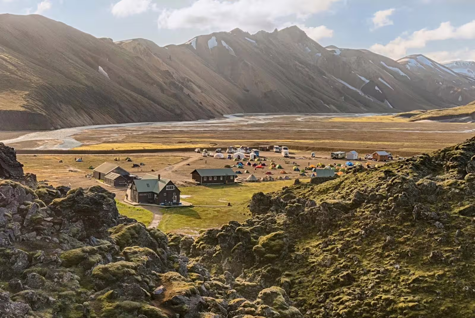 Landmannalaugar campsite with colorful tents, mountain huts, and dramatic Icelandic highlands mountains in background