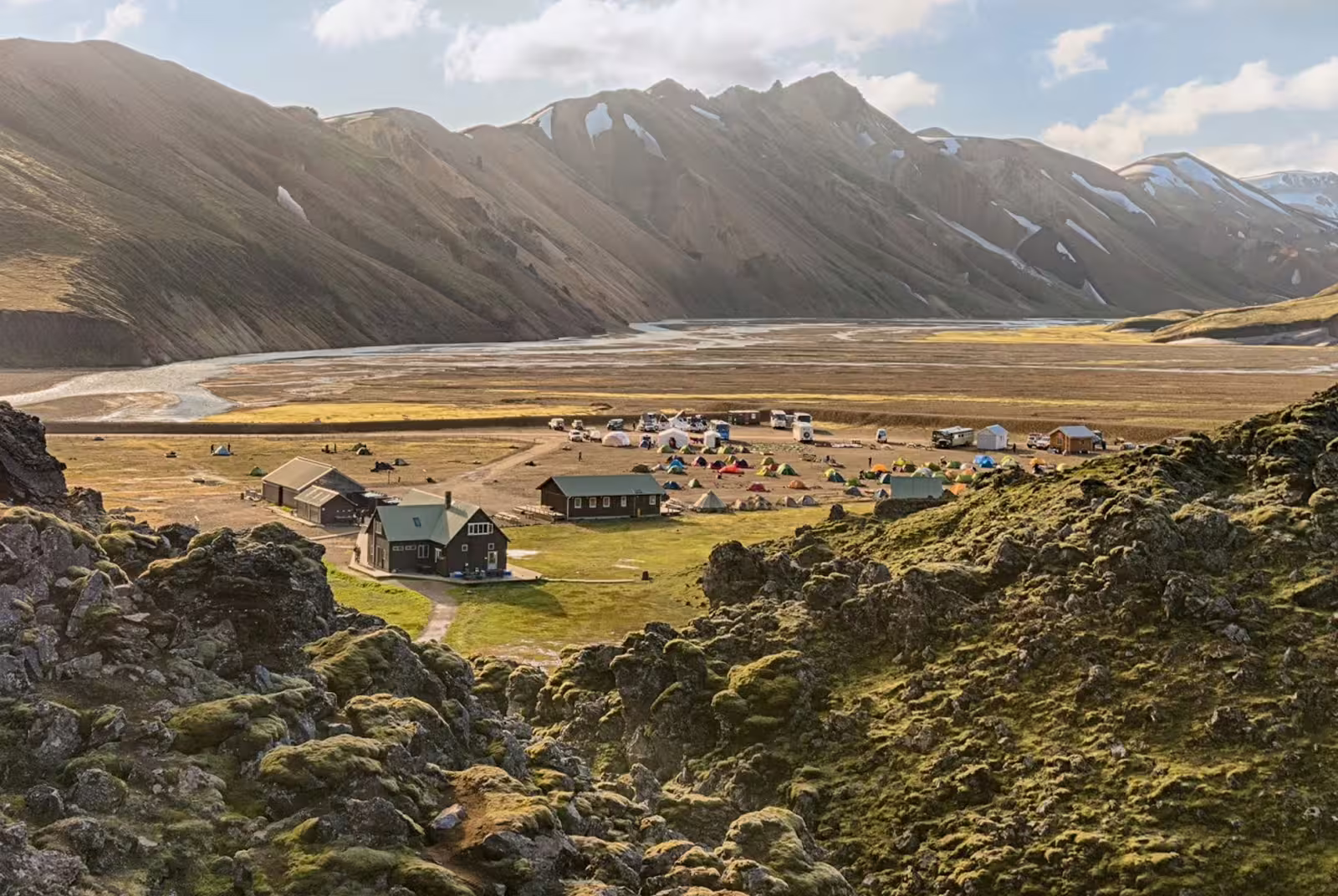 Landmannalaugar campsite with colorful tents, mountain huts, and snow-capped rhyolite mountains in Iceland's highlands