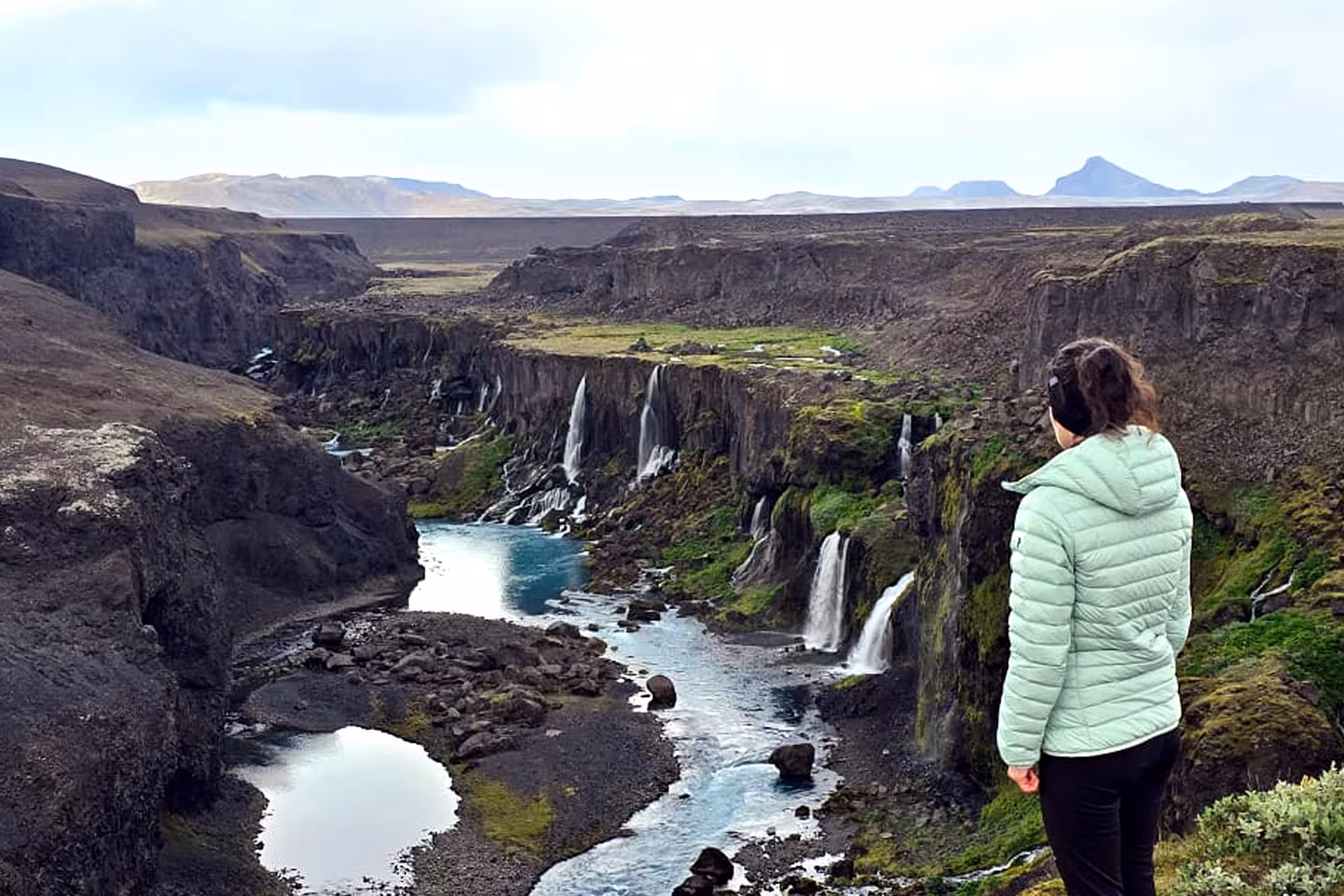 Woman in mint jacket overlooking Sigöldugljúfur canyon with multiple waterfalls in Landmannalaugar, Iceland