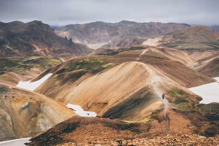 Hiker on a trail through colorful rhyolite mountains of Landmannalaugar with snow patches, Iceland