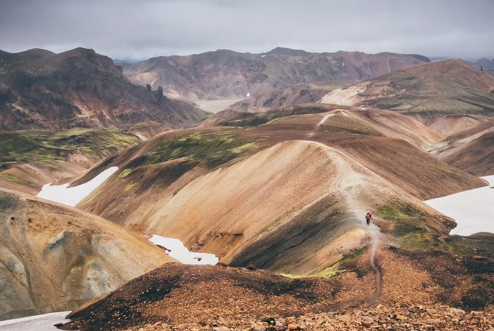 Hikers on a trail through colorful rhyolite mountains of Landmannalaugar with snow patches, Iceland