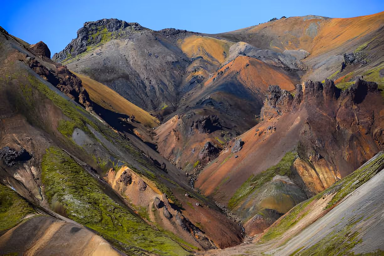 Colorful volcanic mountains of Landmannalaugar with green moss, red and black lava rock under blue sky