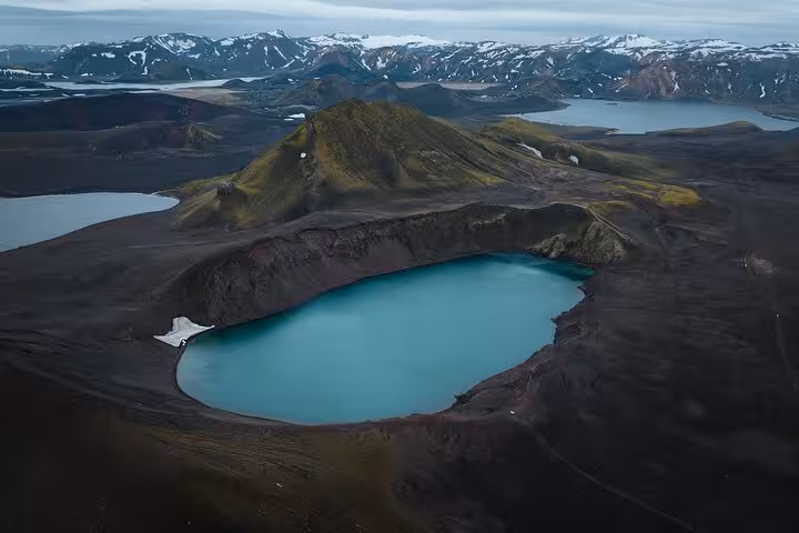 Aerial view of a turquoise crater lake in Landmannalaugar Iceland Highlands with snow-capped mountains