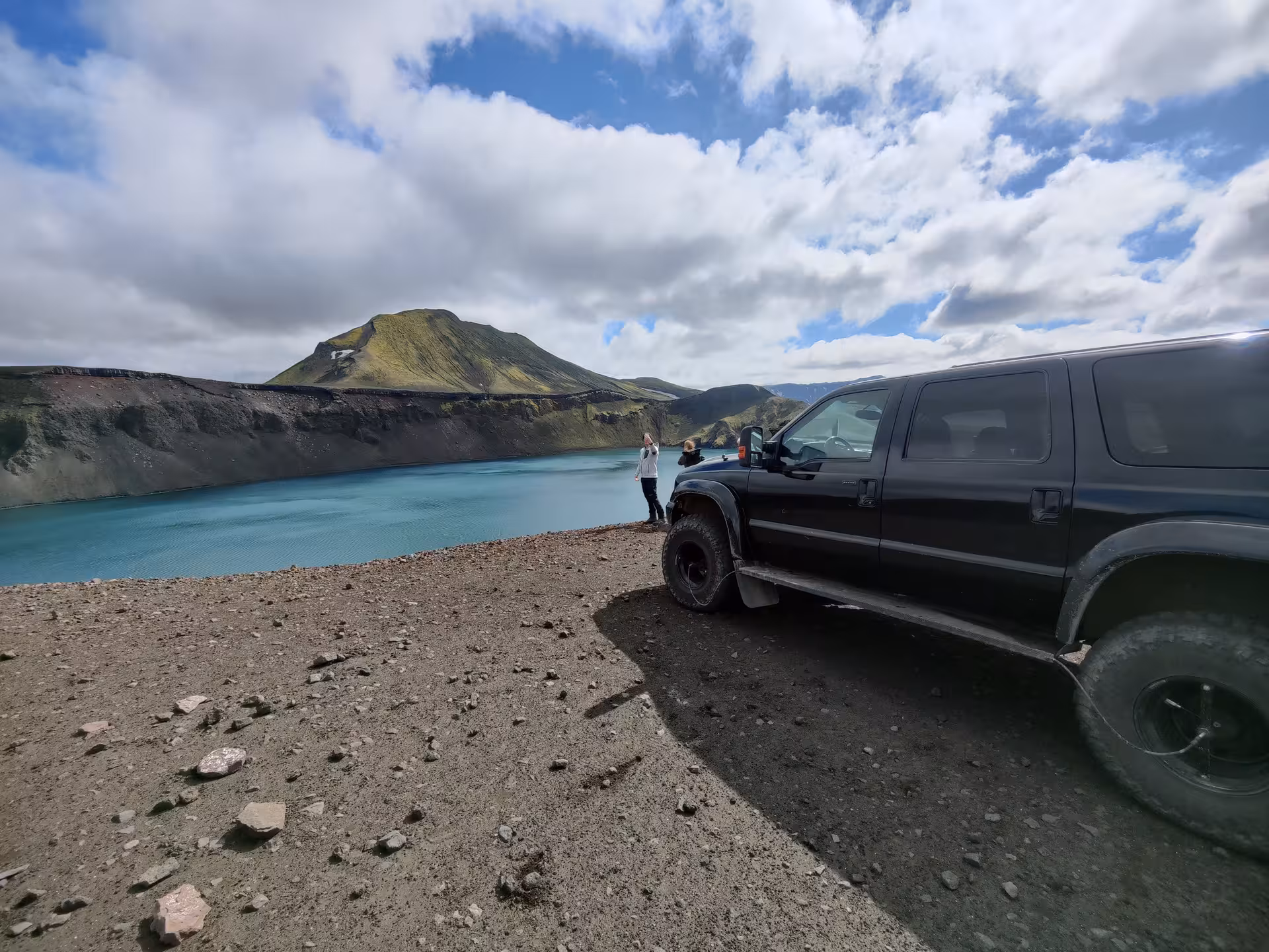 Black 4x4 truck parked at turquoise crater lake in Landmannalaugar highlands Iceland