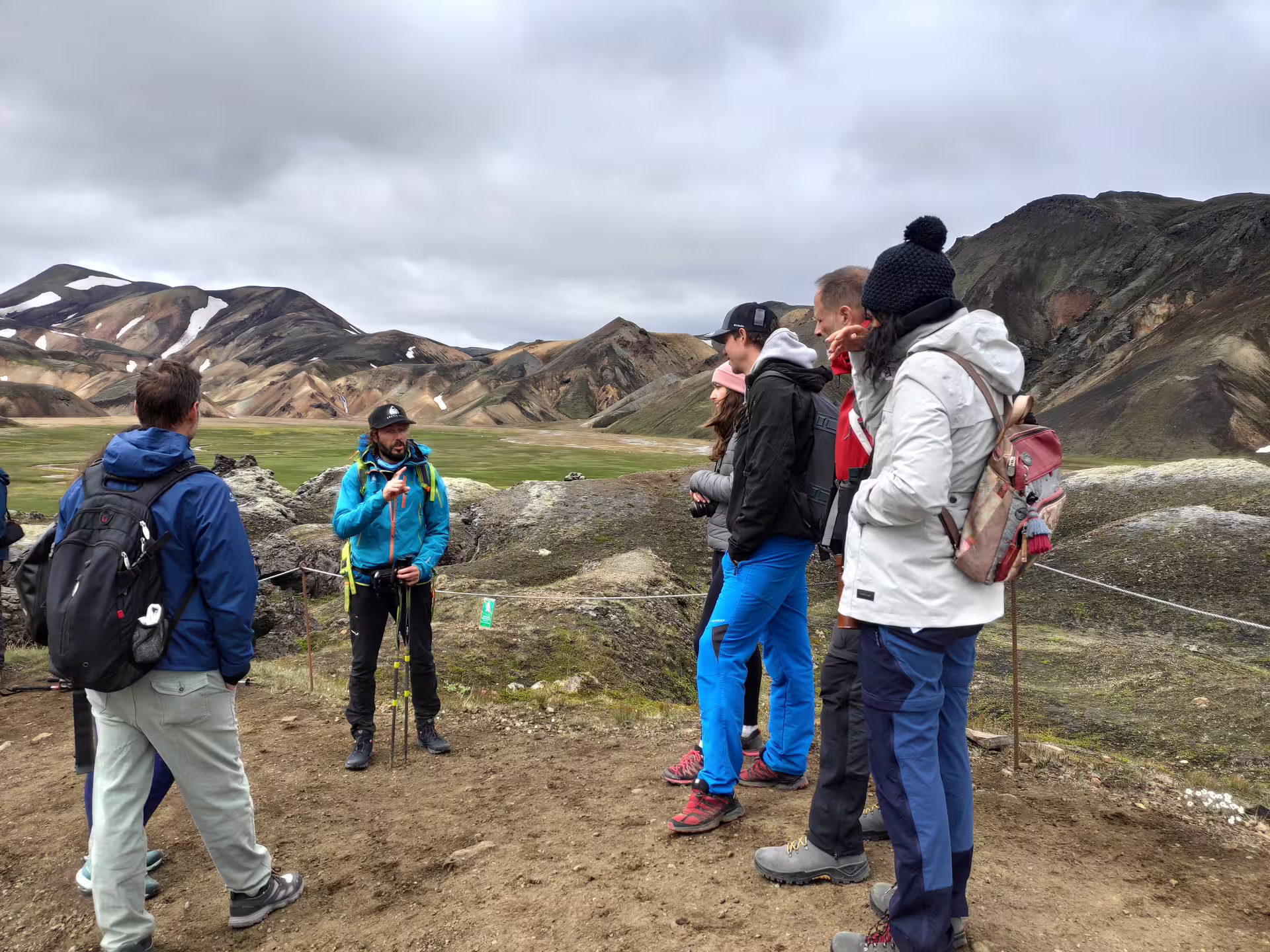 Tour guide briefing hikers at Landmannalaugar with colorful rhyolite mountains in background, Iceland