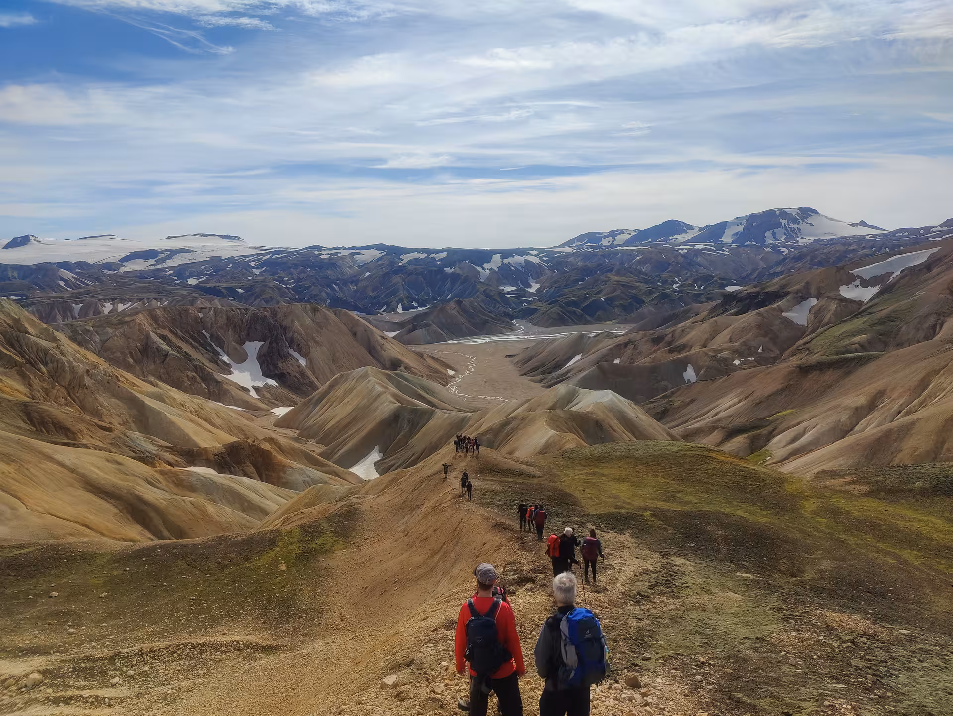 Hikers trekking through colorful rhyolite mountains of Landmannalaugar with snow-capped peaks in background