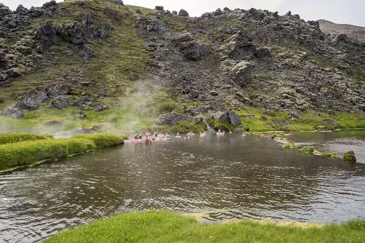 Bathers soaking in a steaming geothermal hot spring pool at Landmannalaugar, Iceland, surrounded by volcanic rocky hills