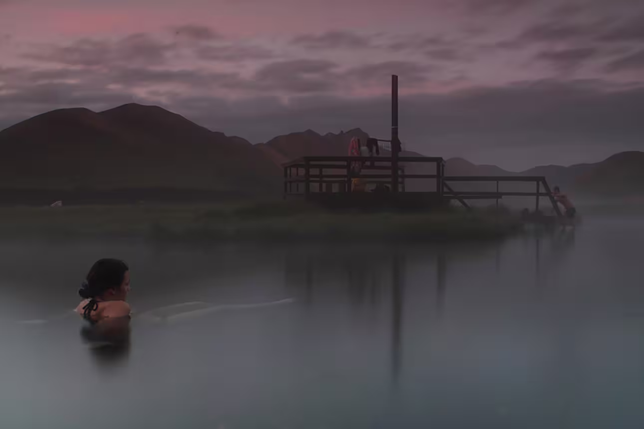 Misty geothermal hot spring at dusk with volcanic mountains and wooden sauna platform in Landmannalaugar