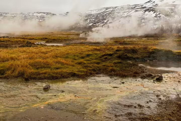 Steaming geothermal vents over mossy lava fields with snow-capped mountains at Landmannalaugar Iceland