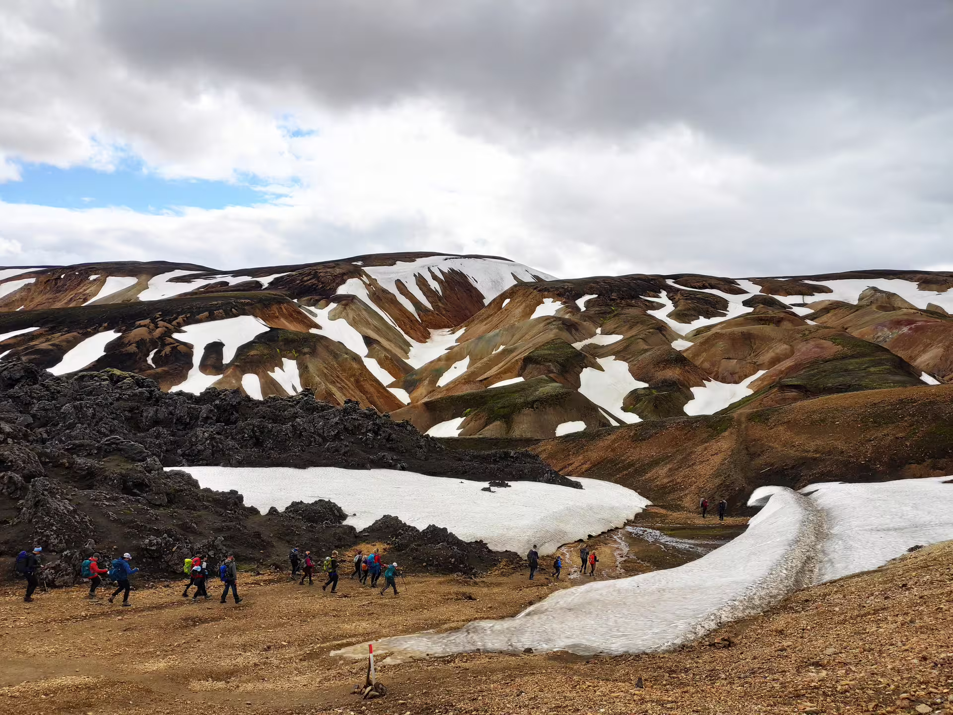 Hikers trekking through Landmannalaugar colorful rhyolite mountains with snow patches in Iceland