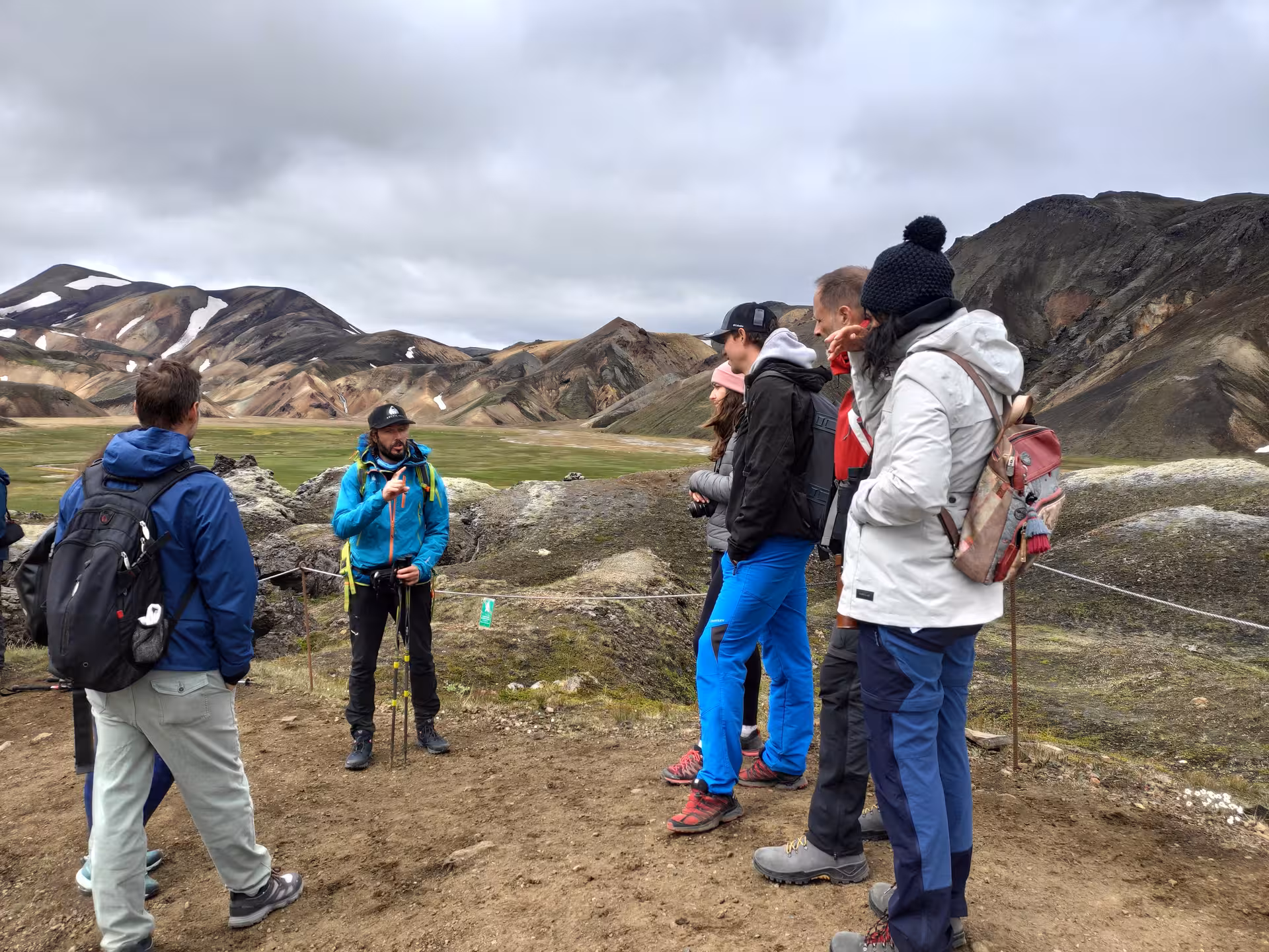 Tour guide briefing hikers at Landmannalaugar with colorful rhyolite mountains in background, Iceland