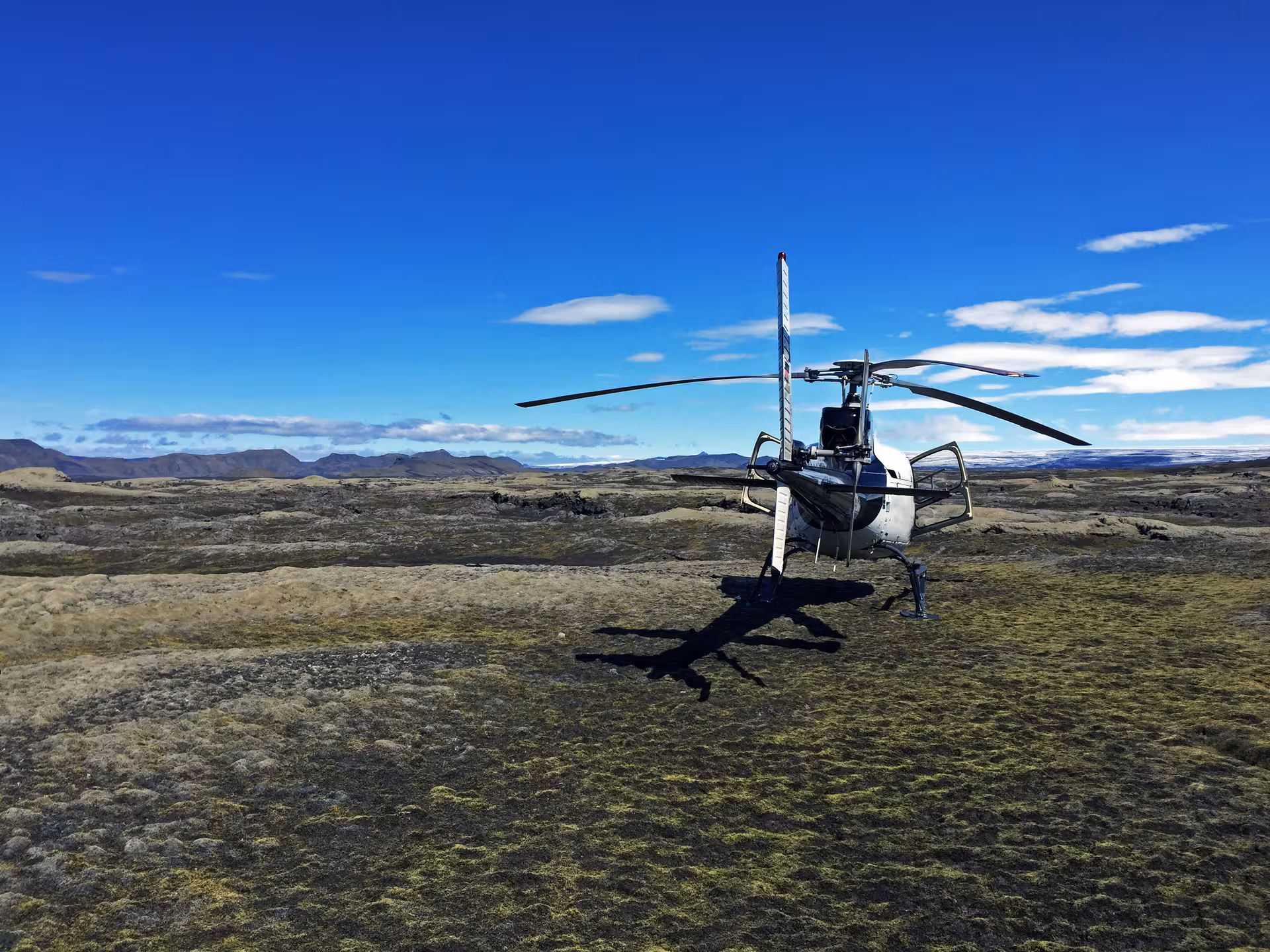 Helicopter landed on mossy lava field in Landmannalaugar Iceland with mountains and blue sky