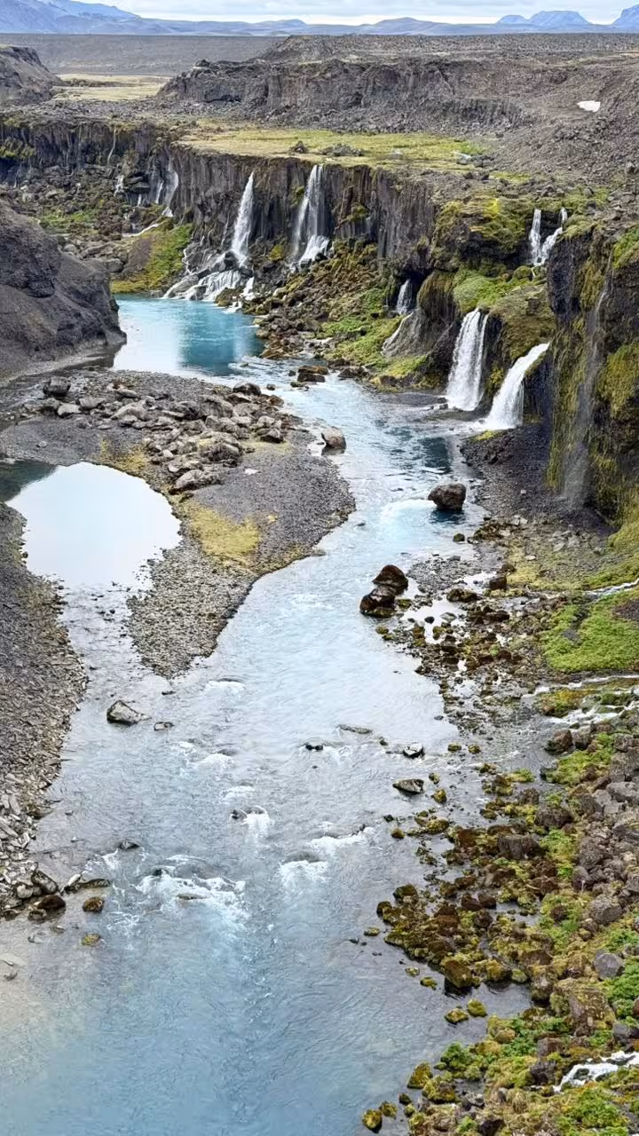 Glacial river canyon with multiple waterfalls cascading down mossy volcanic cliffs in Iceland highlands