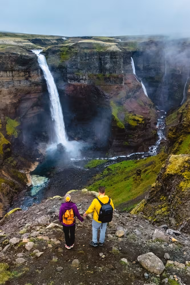 Couple holding hands overlooking dramatic Haifoss waterfall and canyon in Iceland highlands