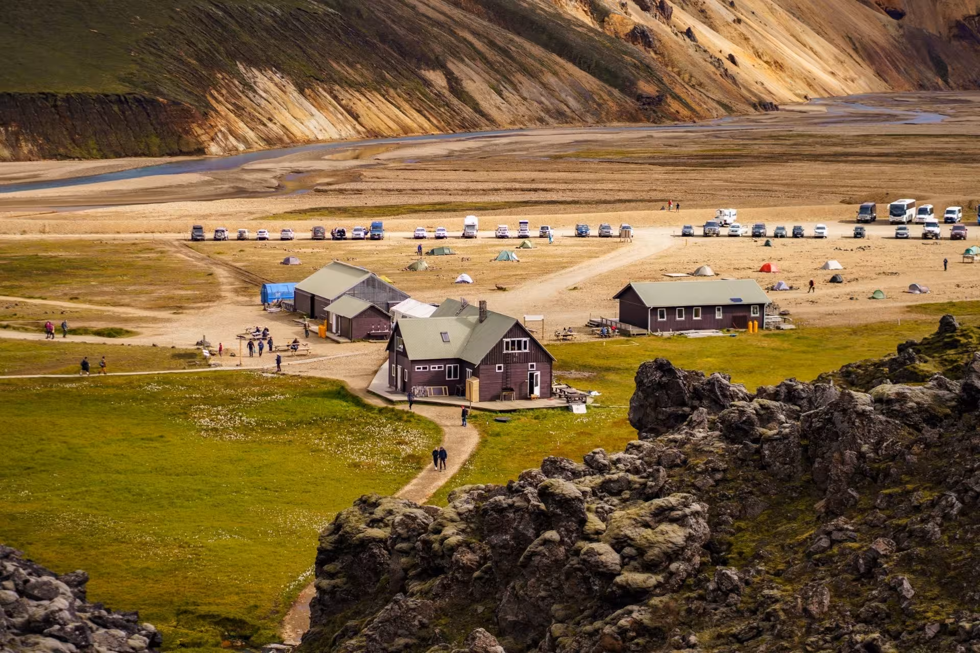 Landmannalaugar highland camp with wooden huts, colorful rhyolite mountains, tents, and visitors in Iceland