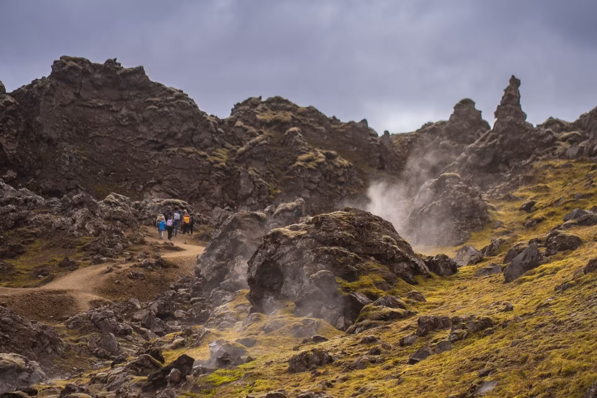 Hikers on a trail through steaming geothermal lava fields and mossy rocks at Landmannalaugar, Iceland