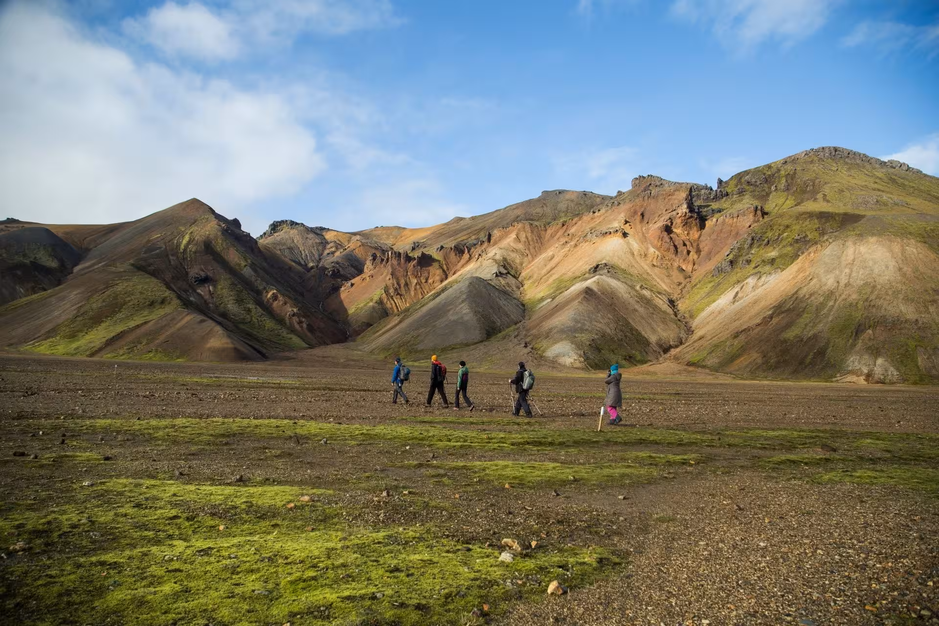 Hikers trekking across volcanic plains toward colorful rhyolite mountains in Landmannalaugar, Iceland Highlands