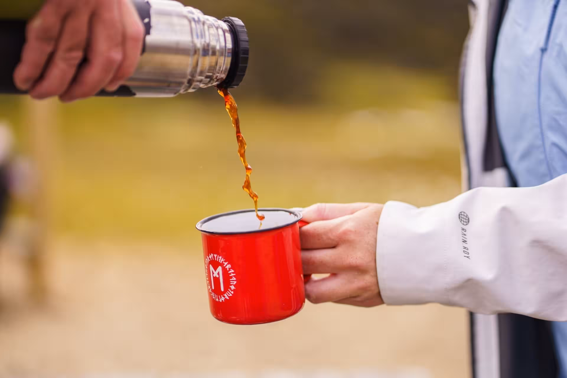 Hot coffee being poured from a thermos into a red enamel camp mug outdoors in the Icelandic highlands