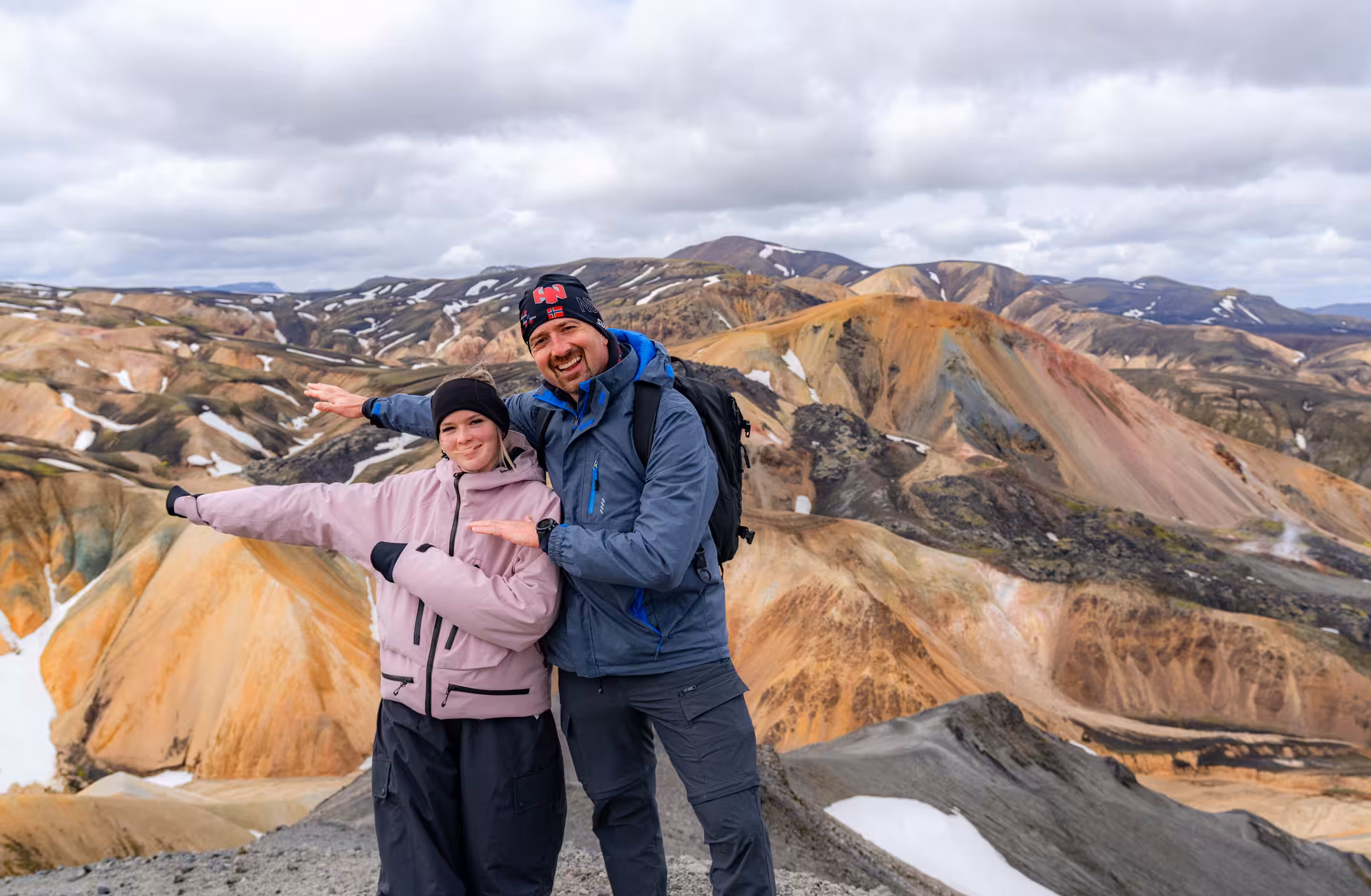 Two hikers posing on a summit with colorful rhyolite mountains of Landmannalaugar highlands behind them