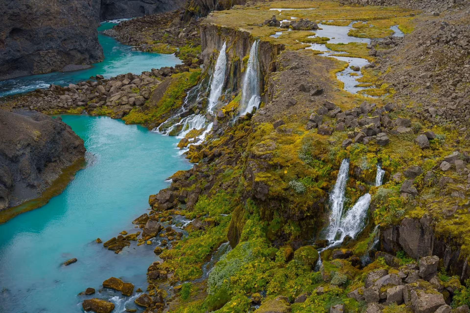 Turquoise glacial river canyon with cascading waterfalls and green moss-covered rocks in Iceland's Highlands