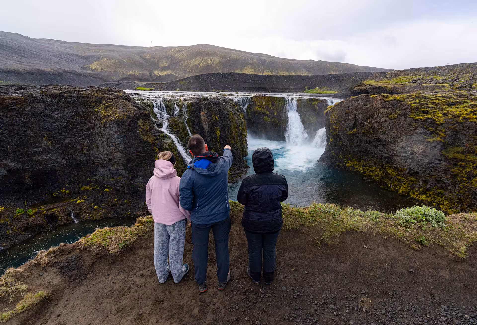 Three tourists overlooking waterfalls and turquoise pools in Landmannalaugar highlands Iceland