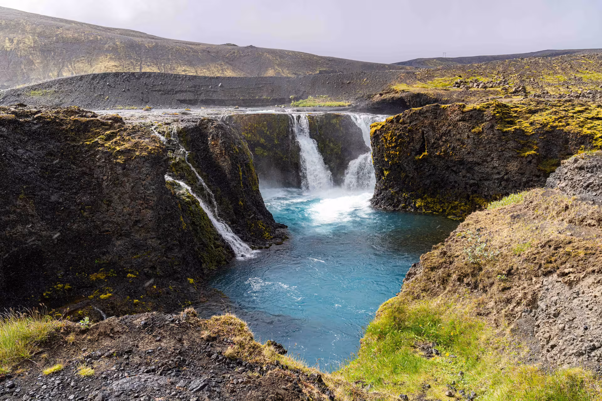 Turquoise glacial pool fed by cascading waterfalls in Landmannalaugar volcanic highlands Iceland