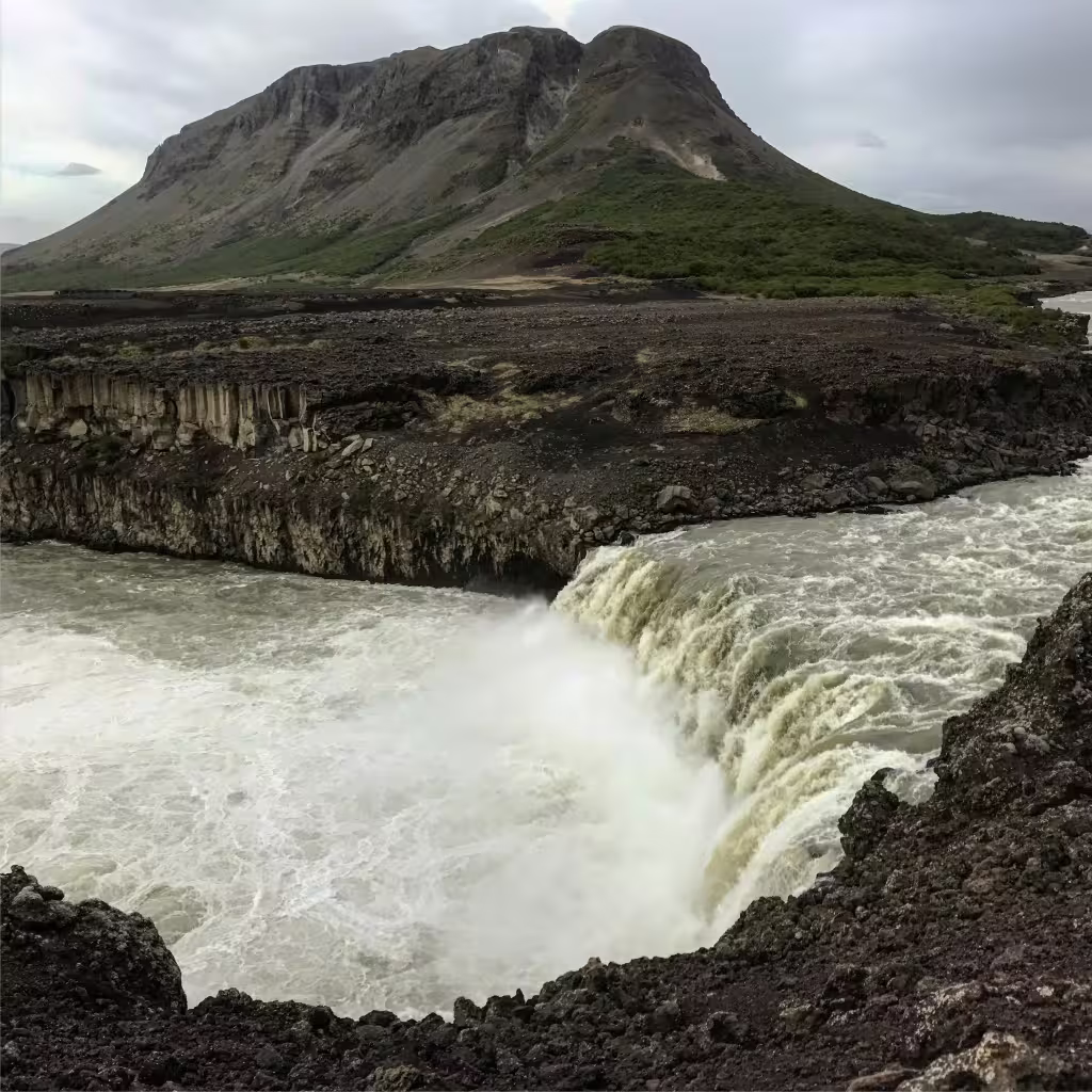 Powerful waterfall cascading over dark basalt cliffs with a volcanic mountain backdrop in Iceland highlands