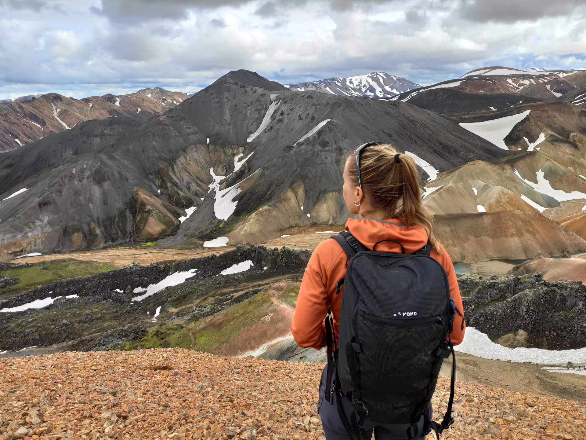 Hiker with backpack overlooking colorful rhyolite mountains and snow patches at Landmannalaugar Iceland