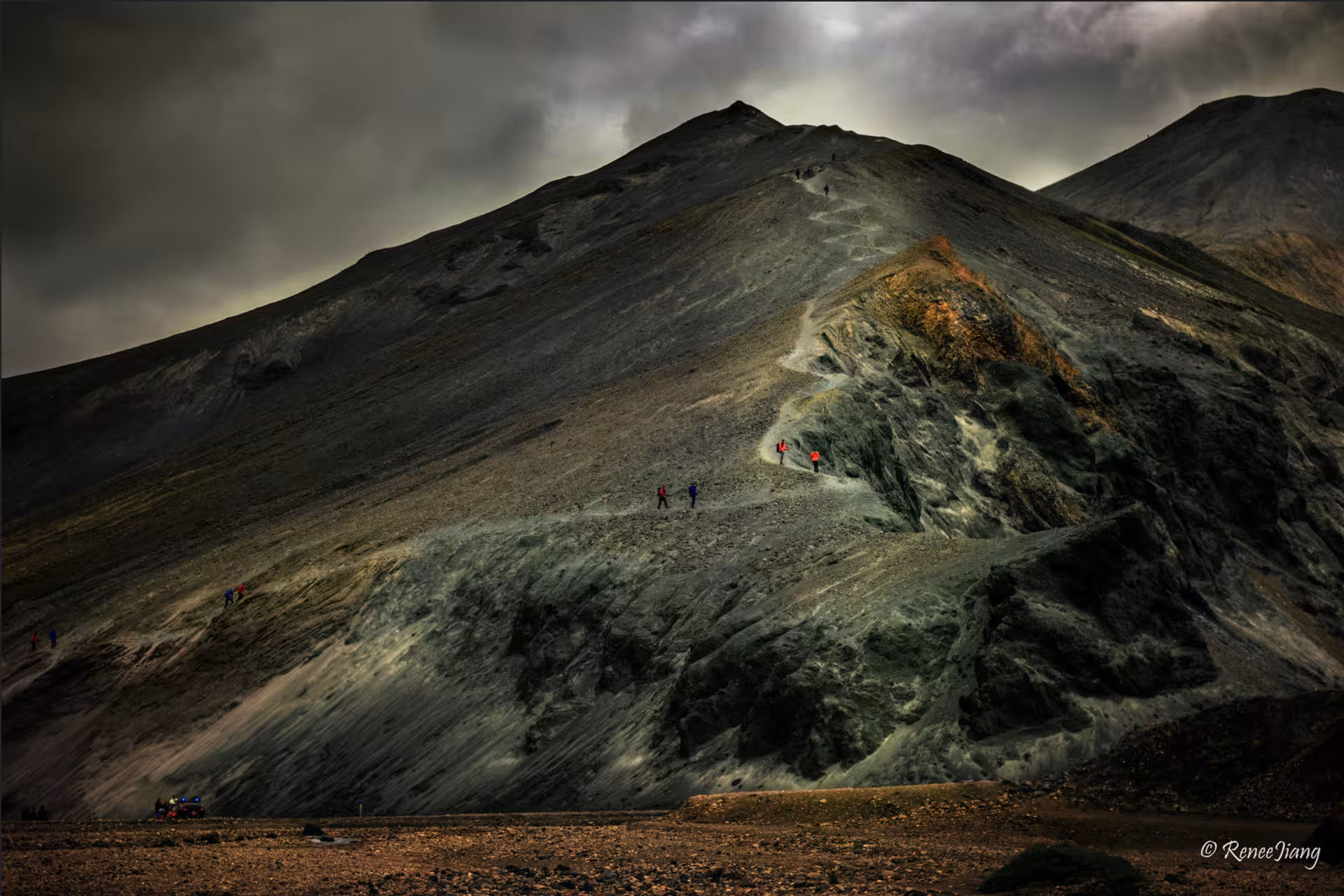 Hikers trekking steep volcanic mountain trail at Landmannalaugar under dramatic stormy skies