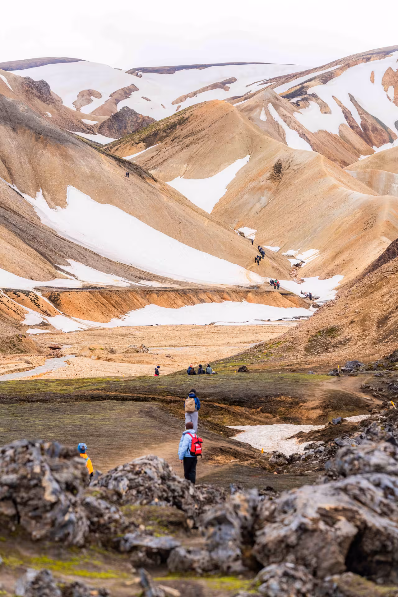 Hikers exploring colorful rhyolite mountains with snow patches at Landmannalaugar, Iceland