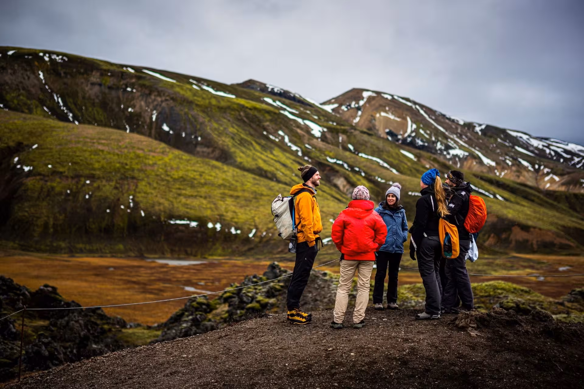 Group of hikers standing on rocky viewpoint overlooking green moss-covered mountains in Landmannalaugar highlands Iceland