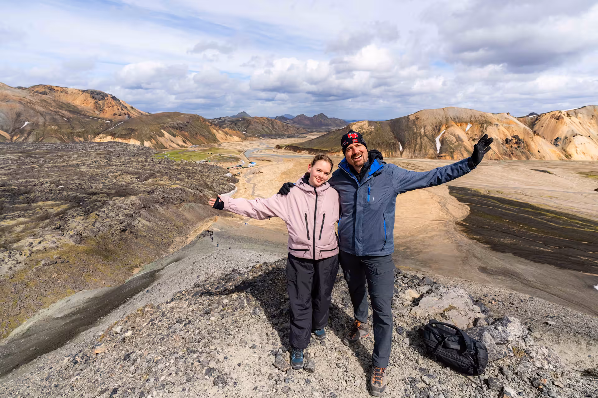 Two hikers celebrating on a mountain summit at Landmannalaugar, Iceland, with colorful rhyolite mountains behind