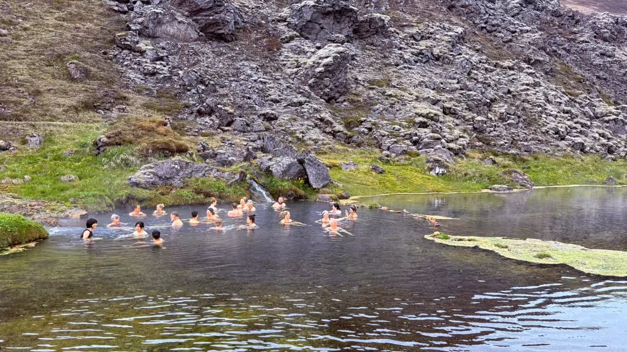 Group of people bathing in Landmannalaugar natural hot spring pool surrounded by volcanic rocks