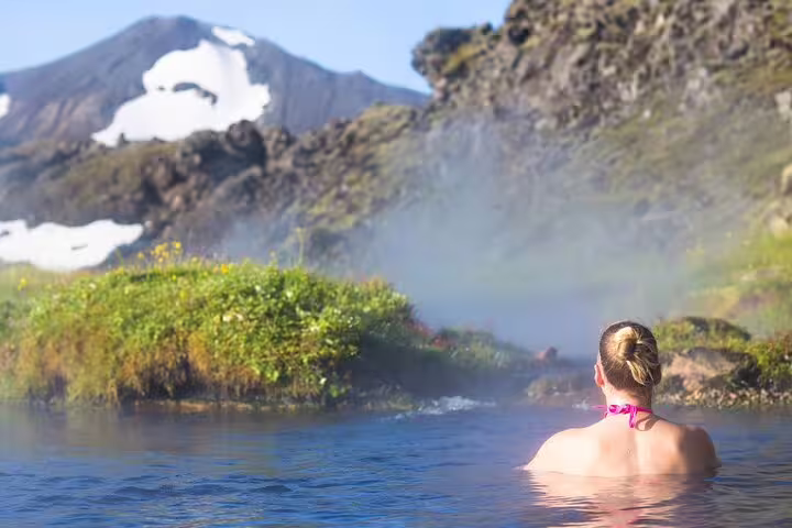 Woman relaxing in Landmannalaugar hot spring with steaming geothermal water and snow-capped volcanic mountains