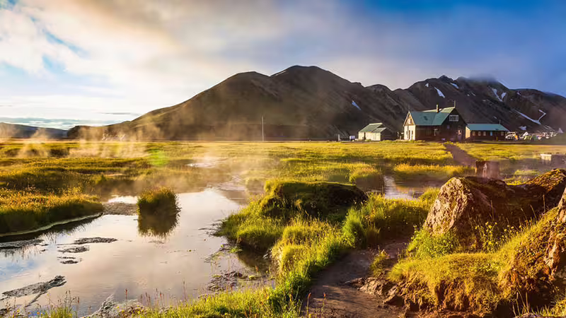 Steaming geothermal hot springs and green wetlands at Landmannalaugar with mountain hut and volcanic peaks