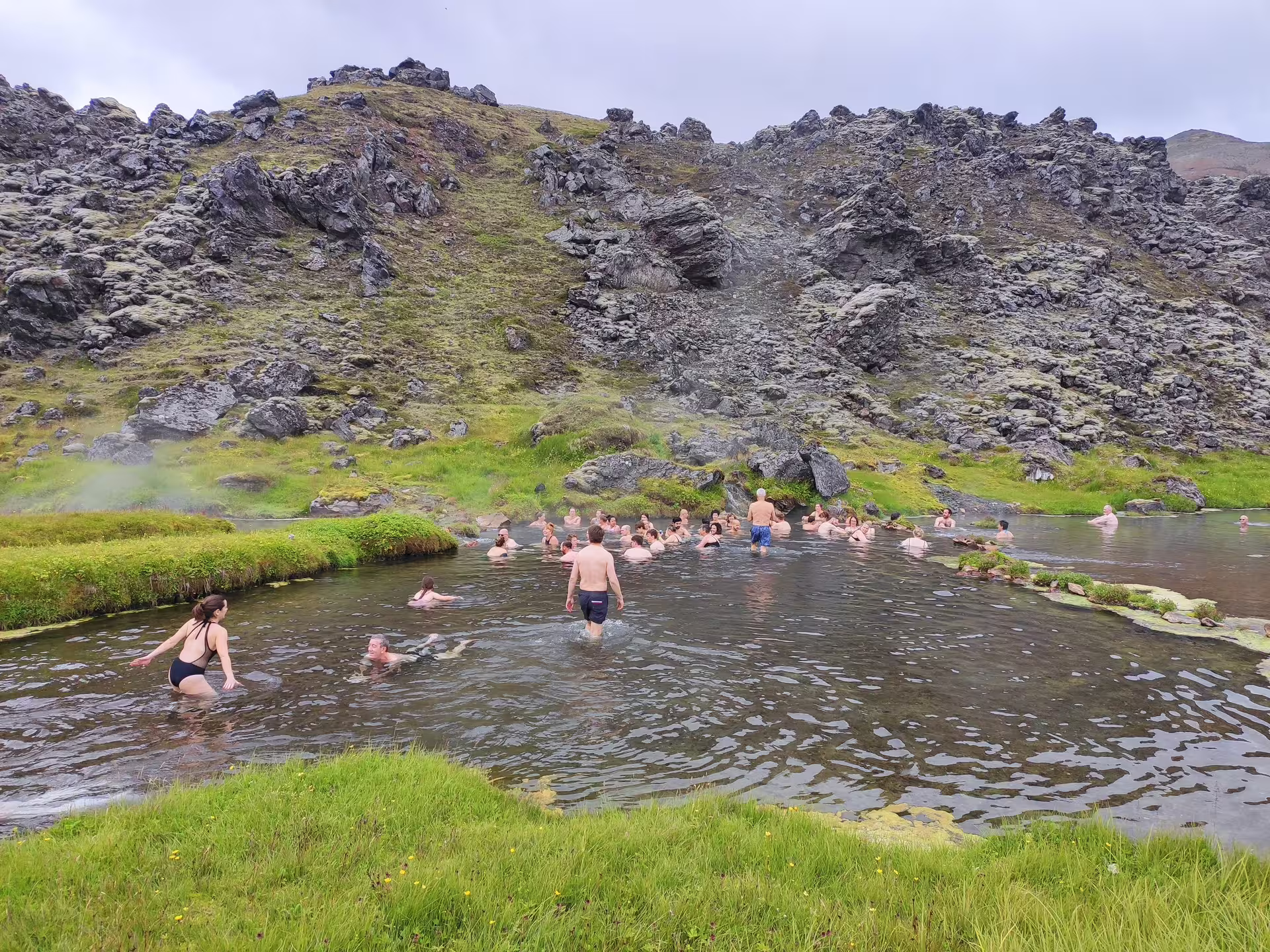 Group of tourists bathing in Landmannalaugar geothermal hot springs surrounded by volcanic rocks Iceland