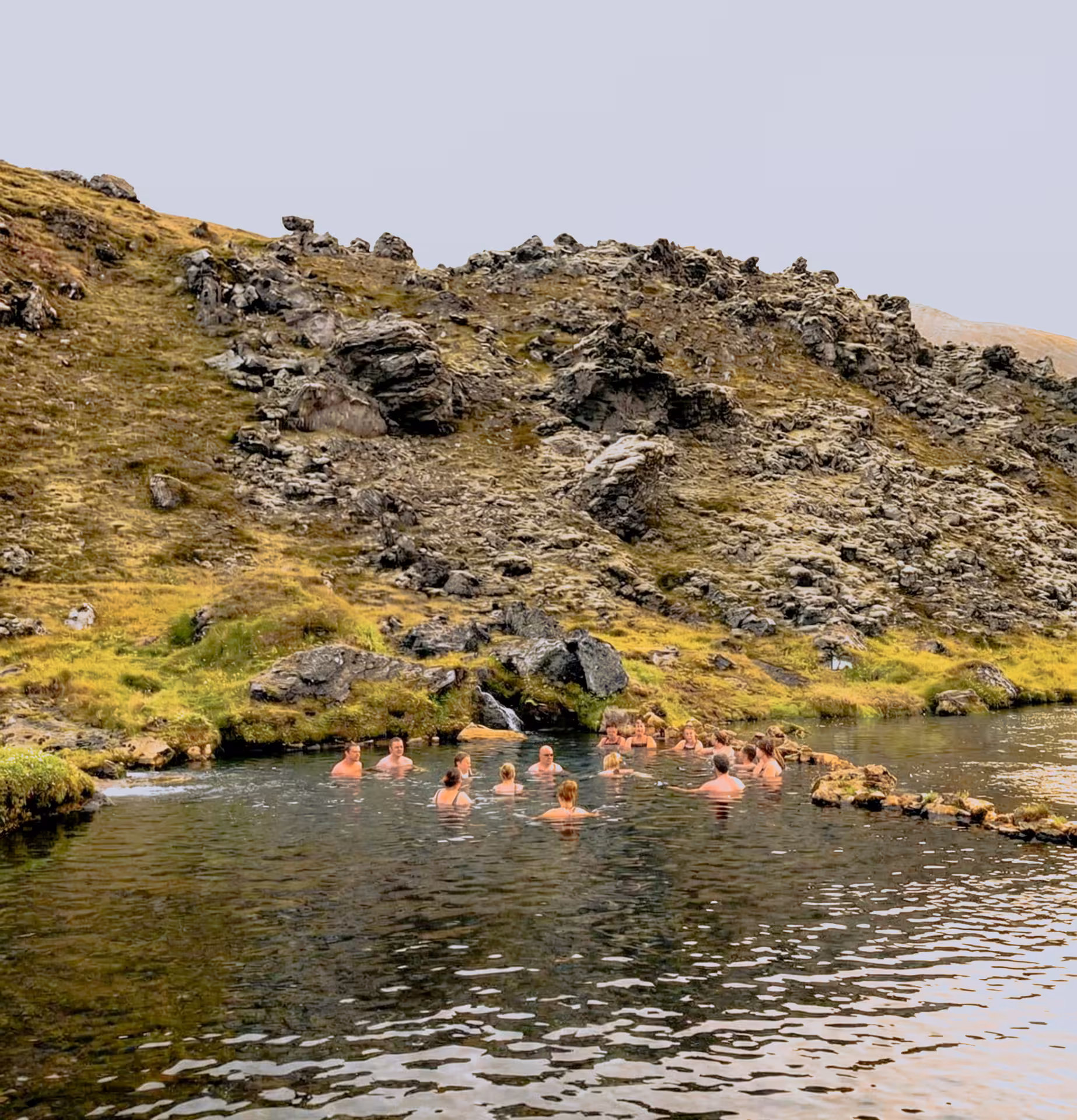 Group of tourists soaking in a natural hot spring pool surrounded by rocky Icelandic highlands at Landmannalaugar