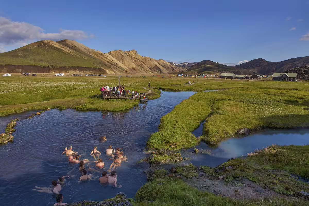 Tourists bathing in Landmannalaugar hot springs with colorful rhyolite mountains in background, Iceland