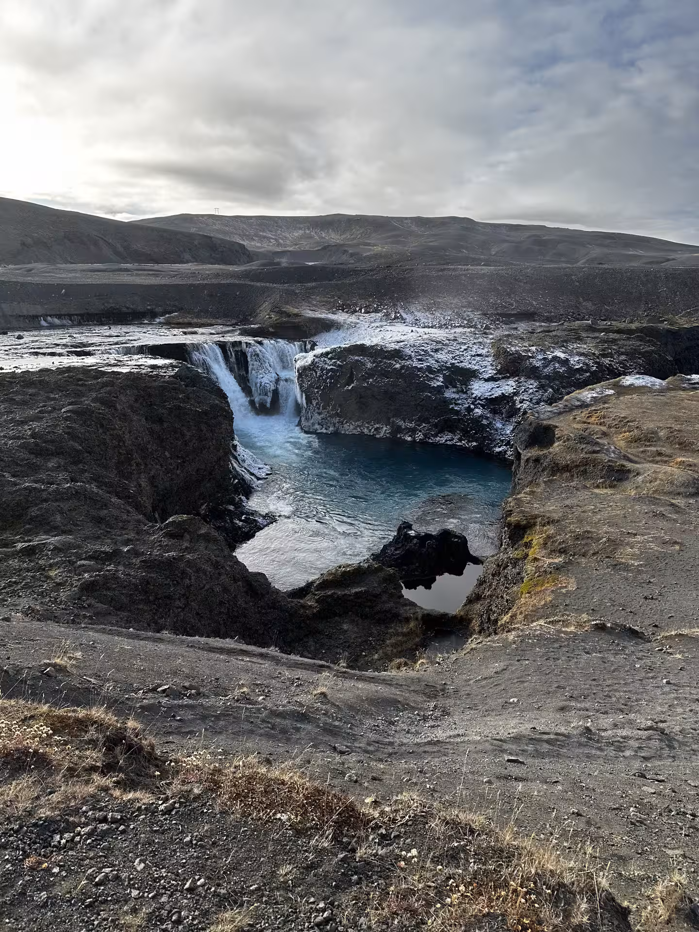 Turquoise glacial waterfall cascading into a rocky canyon in Iceland's Landmannalaugar highlands