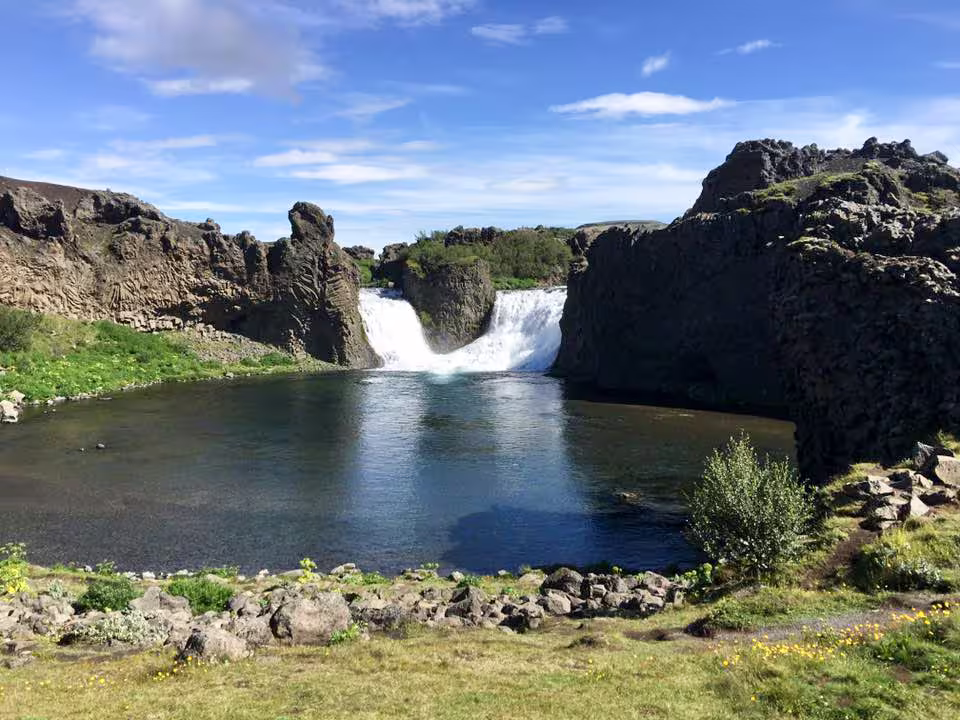 Scenic waterfall cascading into a calm pool surrounded by dark volcanic rocks in Iceland's highlands