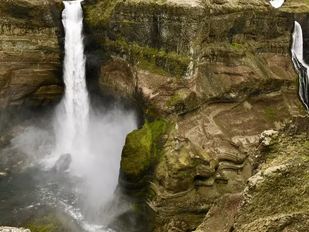 Powerful waterfall cascading into misty gorge with layered volcanic rock formations in Iceland highlands