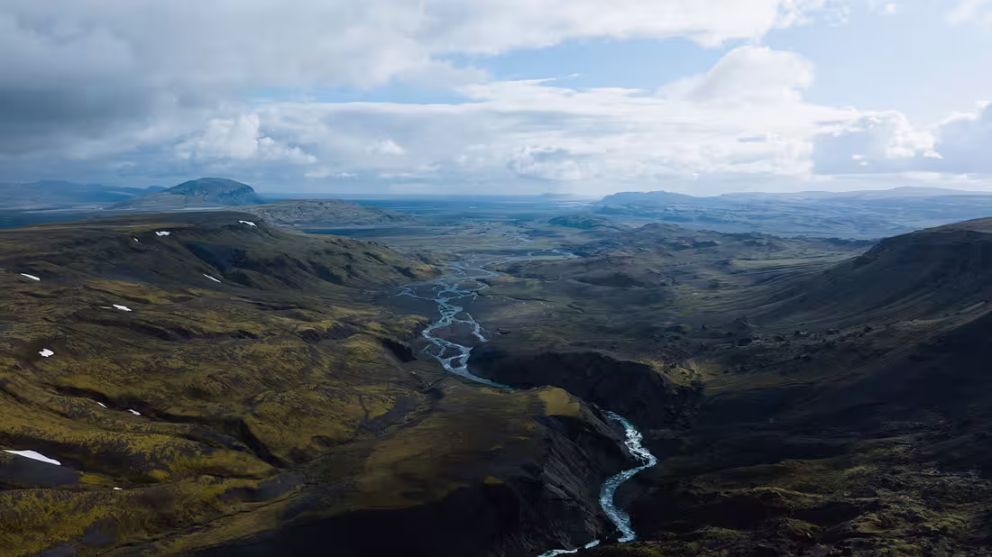 A drone shot of the Icelandic countryside with many hills and a small river running through it