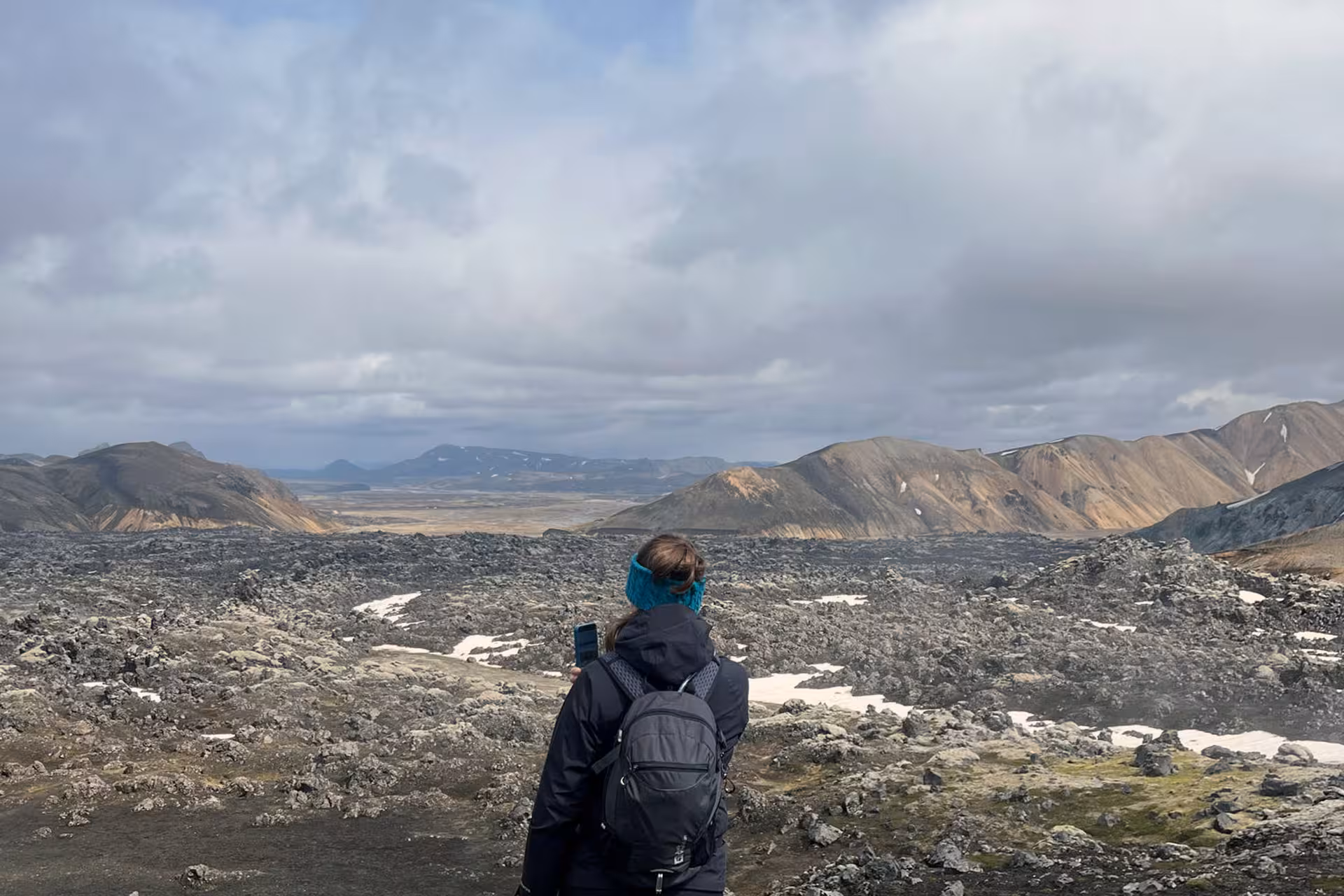 Hiker with backpack overlooking Landmannalaugar lava fields and colorful rhyolite mountains in Iceland