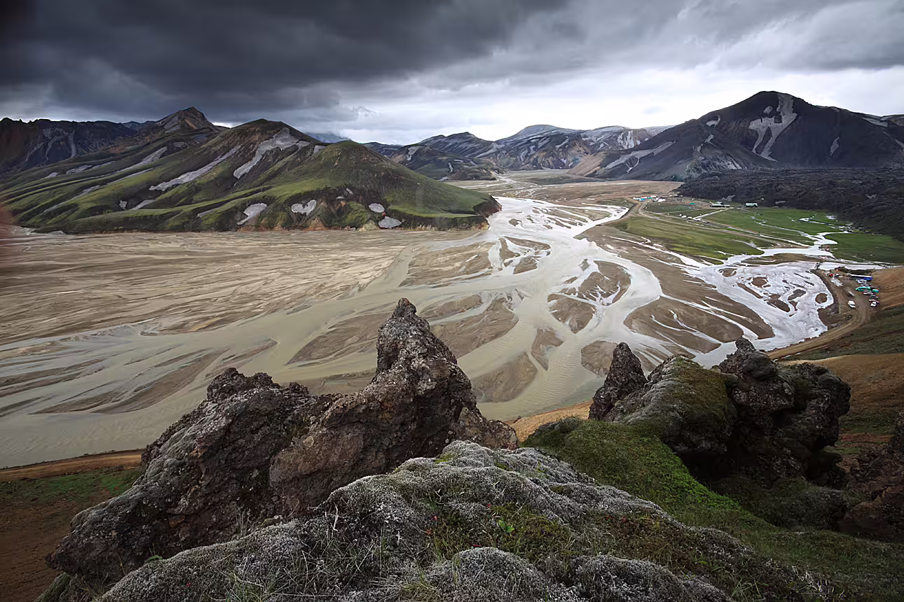 Aerial view of braided glacial river delta in Landmannalaugar surrounded by colorful rhyolite mountains under stormy sky