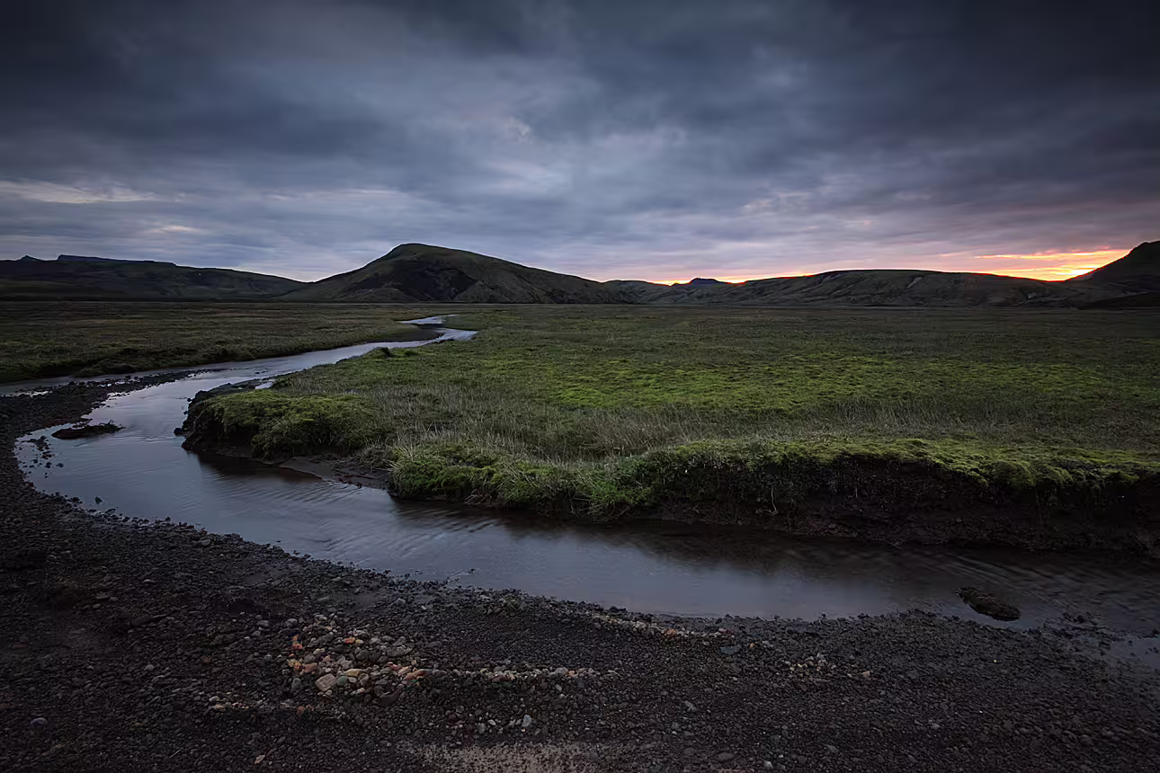 Winding stream through green meadows at sunset with volcanic mountains in Landmannalaugar, Iceland