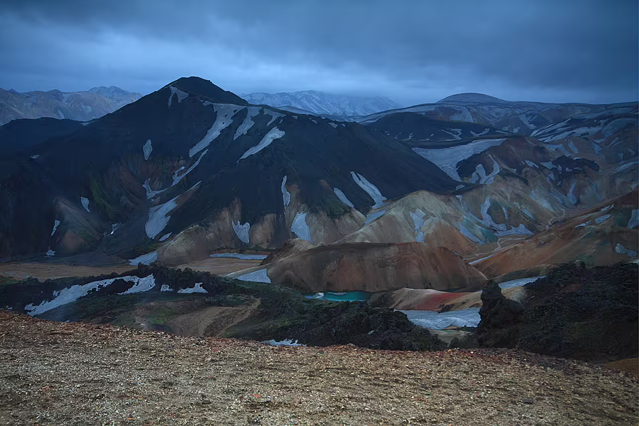Colorful rhyolite mountains with snow patches and turquoise lakes at Landmannalaugar under dramatic cloudy sky