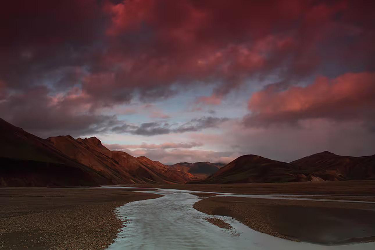 Braided glacial river winding through Landmannalaugar mountains under dramatic red sunset sky